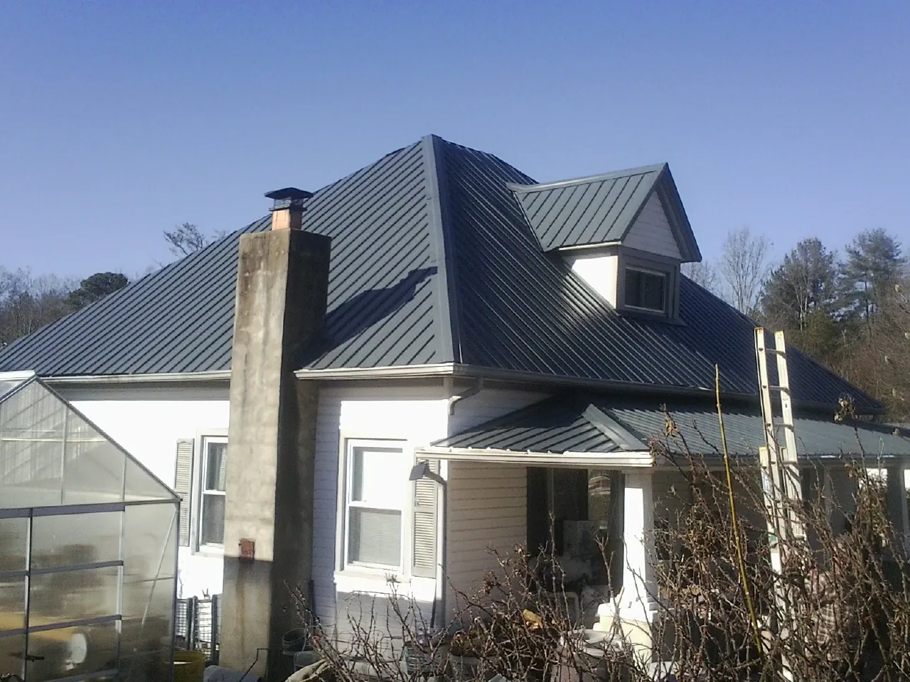 Dark blue standing seam metal roof on a white farmhouse with dormer — Slate & Tile Roof Repair by Roofing Brothers in Buckeye