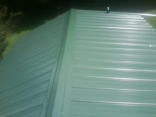 New green metal panels meeting at the ridge of a roof — Flat Roof Repair work by our crew in Buckeye